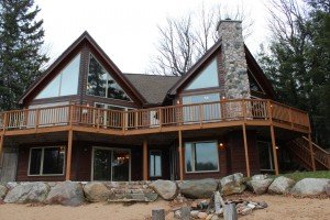 A view of the back of the house with massive bay windows, stone fireplace and large upper deck
